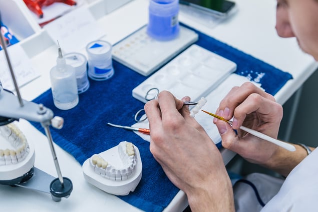 Trabajo manual sobre una restauración dental junto a modelos de laboratorio